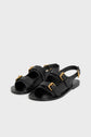 A pair of black leather sandales plates with three gold buckles on each sandal, including an ankle strap. These elegant sandales cuir feature an open toe and flat sole, displayed on a plain light gray background.