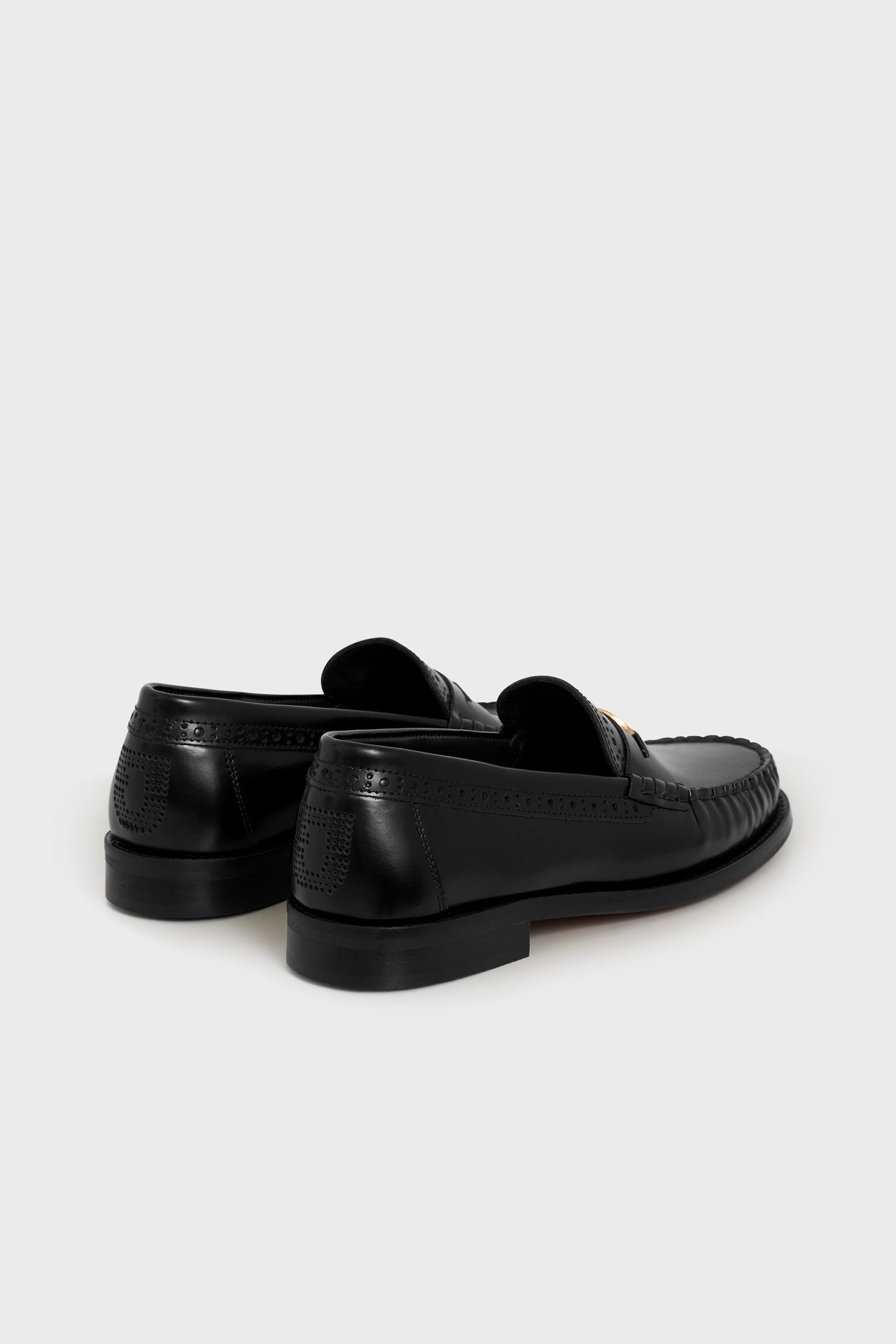 A pair of mocassins noirs cuir with stitching details, viewed from the back and side on a light gray background, showcasing their elegant and timeless style.