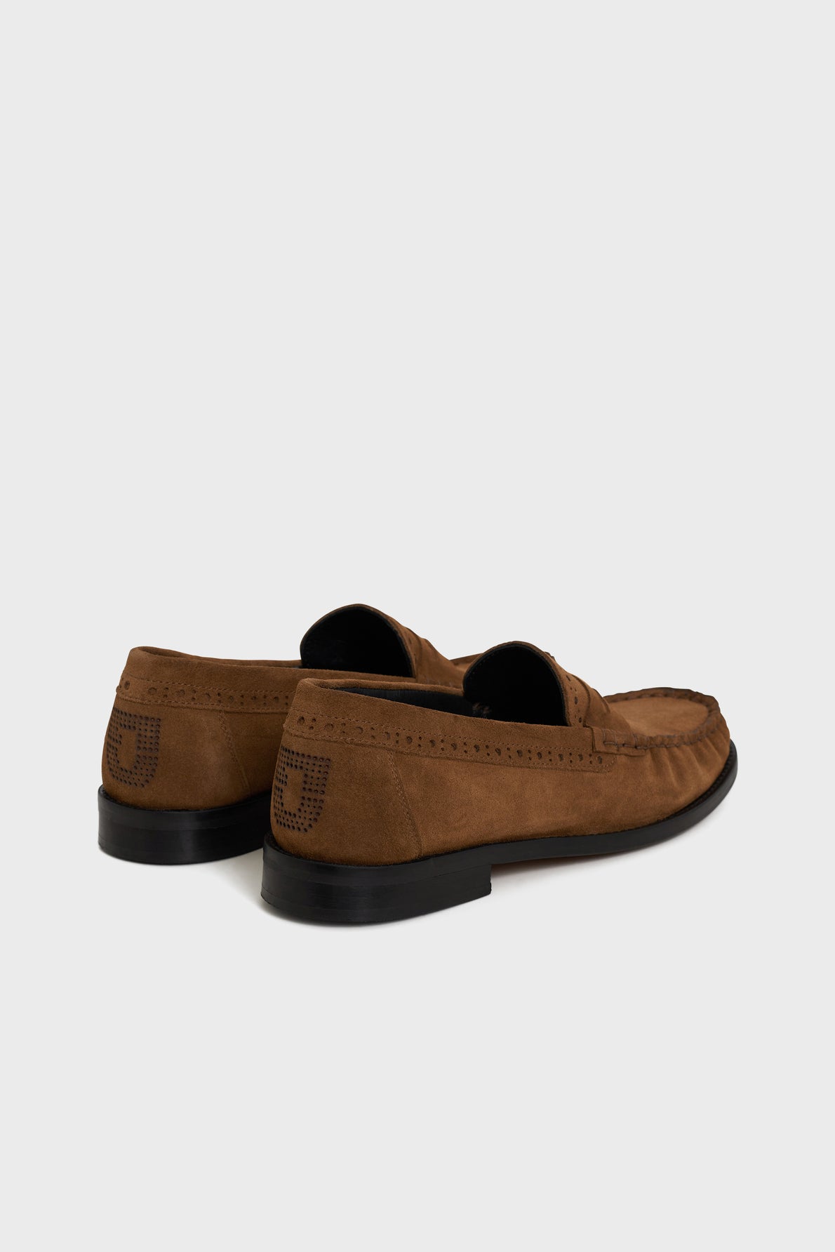 A pair of brown suede loafers with black rubber soles, viewed from the back and side, featuring a stitched design on the heel—these mocassins cuir velours are perfect for those seeking chaussures casual chic.