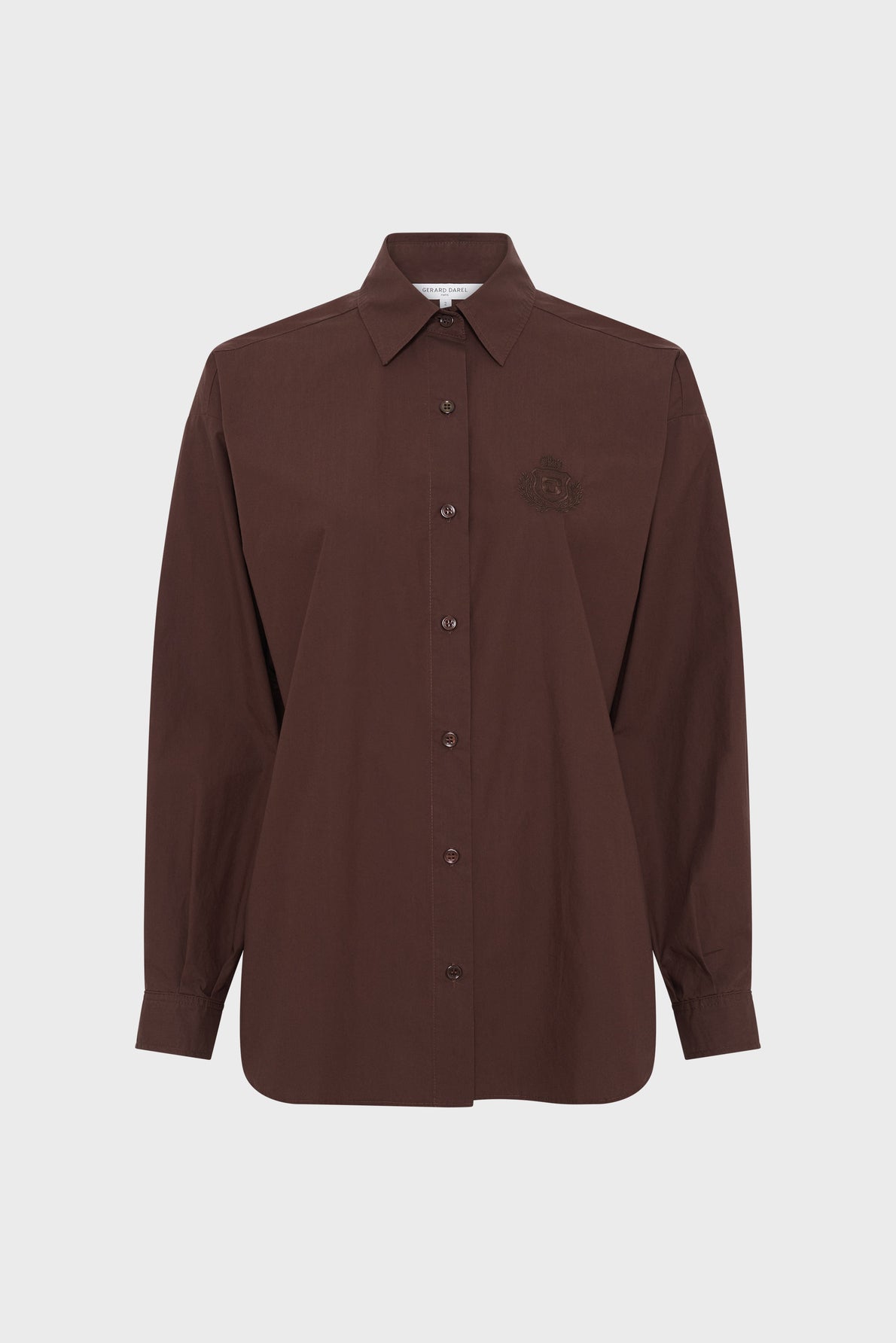 A long-sleeved, button-up, dark brown chemise en popeline with a collar and a subtle blason brodé on the left chest, crafted from soft coton uni and displayed against a plain white background.