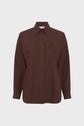 A long-sleeved, button-up, dark brown chemise en popeline with a collar and a subtle blason brodé on the left chest, crafted from soft coton uni and displayed against a plain white background.