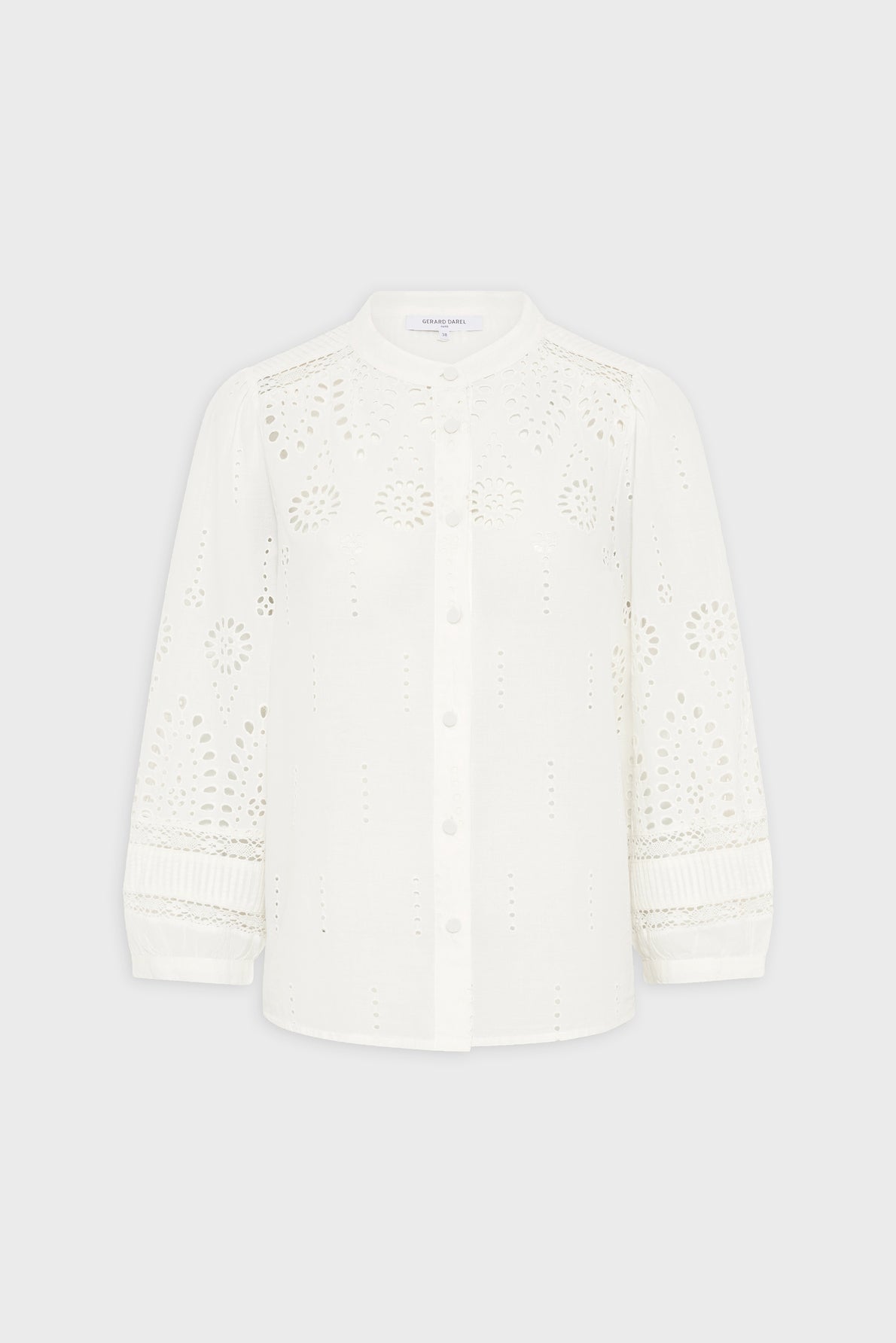 White, long-sleeve button-up blouse with intricate eyelet embroidery, round neckline, and slightly puffed sleeves. The blouse has a delicate, airy design and the embroidery creates floral patterns on the fabric.