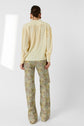 A person stands facing away, wearing a blouse jaune in light yellow crêpe soie with manches bouffantes and loose, patterned pants featuring green and yellow tones, against a plain white background.