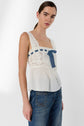 A woman wearing an esprit lingerie-inspired white lace sleeveless top court with a blue ribbon and blue jeans stands against a plain light gray background.