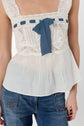 A person wearing a white lace sleeveless top court with a blue ribbon bow and blue jeans, shown from shoulders to hips against a plain background in an esprit lingerie style.