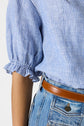 A person wearing a blue and white striped short-sleeve blouse à rayures with ruffled cuffs, paired with high-waisted blue jeans and a brown leather belt.