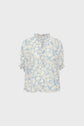 Light blue blouse fluide à manches courtes, ornée d’un motif floral off-white, avec col montant et bords de manches volantés, présentée sur un fond blanc uni.
