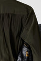 Close-up of the back of a dark green shirt with gathered fabric near the shoulder, next to a black leather bag with a gold buckle.