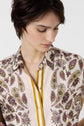 A person with short dark hair looks down, wearing a cream-colored shirt with a paisley pattern in purple, yellow, and brown, and yellow trim along the button line.