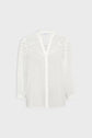 White long-sleeve blouse with a V-neckline, subtle lace details across the chest and shoulders, button-down front, and slightly gathered cuffs. The fabric appears light and semi-sheer, bringing a delicate touch of tissu transparent to the overall design.