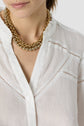 Woman wearing a sheer white chemise brodée with decorative stitching and two chunky gold necklaces. The image is cropped to show her from the nose down to the chest.