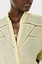 A person wearing a light yellow blouse crafted from tissu fin with delicate lace details and a gold necklace with a round pendant. The photo is cropped at the nose and upper chest.