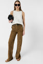 Woman wearing sunglasses, a white sleeveless top, brown wide-leg pants with a black belt, and sandals holds a black clutch against a plain white background.