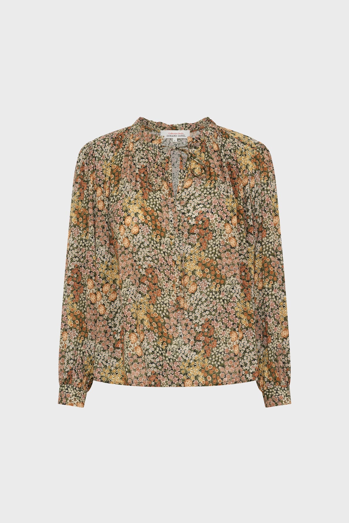 Long-sleeved floral blouse with a v-neck and buttoned cuffs, featuring a delicate imprimé floral of small flowers in shades of pink, orange, green, and white on a light background. The blouse Carinne is displayed on a plain white surface.