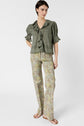 A woman stands wearing a green ruffled blouse, floral print flared pants, and sandals against a white background.