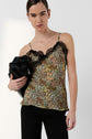 Person wearing a floral camisole with lace trim and black pants, holding a black bag under one arm, standing against a plain light background.