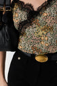 A person wearing a black belt with a large gold oval buckle, high-waisted black pants, and a floral lace-trimmed top, carrying a black bag on their shoulder.
