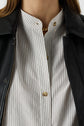 Close-up of a person wearing a chemise à rayures blanche, style col mao, accented with a gold necklace and topped with a black leather jacket. Only the lower face and upper torso are visible.