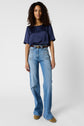 A person stands against a plain background wearing a navy short-sleeve top, high-waisted light blue wide-leg jeans, a belt, and tan shoes.