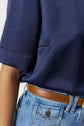 A person wearing a navy blue short-sleeve shirt tucked into high-waisted light blue jeans with a brown leather belt.