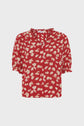 Red blouse with a white and yellow daisy print, inspired by the classic chemise fleurs style. Featuring short manches bouffantes with ruffled cuffs and a charming col volanté, this blouse has a button-down front and a loose, relaxed fit.
