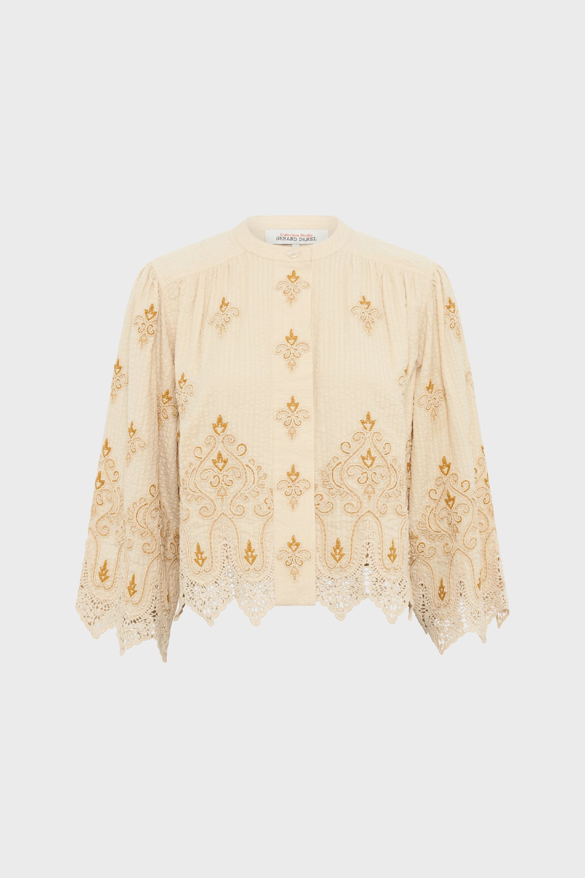 Cream-colored, long-sleeve embroidered blouse with gold floral patterns and a scalloped hem, crafted from coton seersucker for a softly textured feel, displayed on a plain white background. This édition limitée piece combines elegance and comfort in every detail.