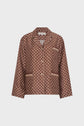 Brown pajama-style chemise satinée with a white geometric pattern and beige trim on the collar, cuffs, pockets, and button placket, featuring a subtle monogramme GD detail, displayed against a plain white background.