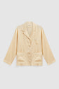 A light beige, long-sleeve chemise col tailleur satin pajama top with a notched collar, chest pocket, two lower front pockets, and button-down front, displayed on a plain white background.