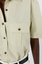 A close-up of a person wearing a light yellow short-sleeved button-up shirt with a chest pocket and black buttons, tucked into white pants with a black belt, gives off the casual elegance reminiscent of a chemise manches courtes.