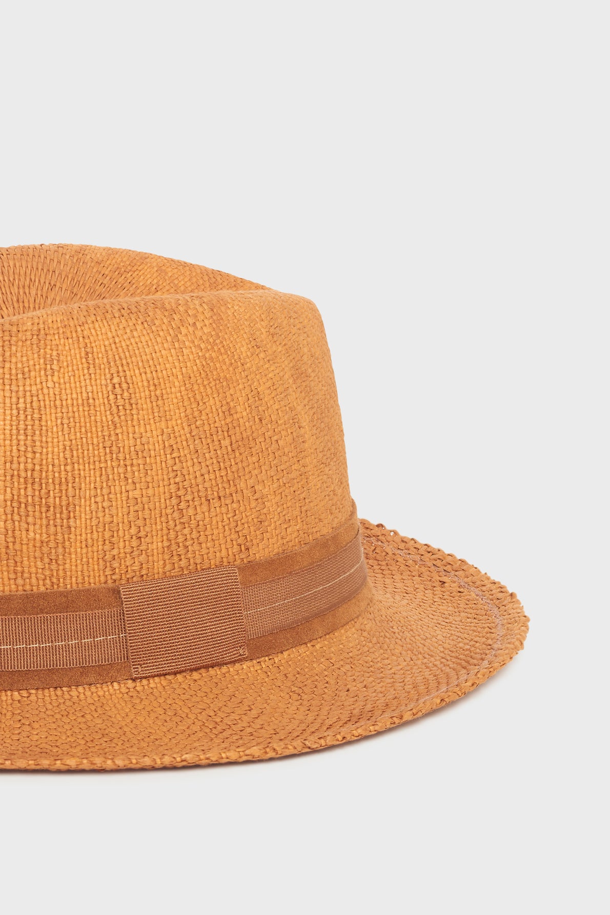 A close-up of a light brown chapeau en paille fedora hat with a matching brown ribbon band, displayed against a plain white background—the perfect accessoire vacances for sunny getaways.