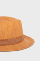 A close-up of a light brown chapeau en paille fedora hat with a matching brown ribbon band, displayed against a plain white background—the perfect accessoire vacances for sunny getaways.