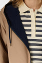 A person wearing a beige parka mi-saison over a cream polo shirt with black horizontal stripes. The parka is unzipped, revealing the shirt’s buttons and collar. Only the upper torso is visible.