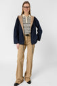 A person wearing glasses, a navy and tan parka mi-saison hooded jacket, a striped shirt, beige pants with side details, and black shoes stands against a plain white background.