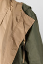 Close-up of a parka mi-longue with a beige inner lining and an olive green outer layer, featuring a drawstring and metal eyelet on the hood.