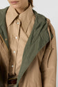A person wearing a tan button-up shirt with a wide collar and a tan and green veste mi-saison layered over it. Only the lower face and upper torso are visible.