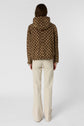 Person standing facing away, wearing a brown parka courte with a white geometric monogramme écru pattern and cream-colored wide-leg pants, against a plain light background.