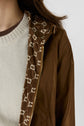 A close-up of a person wearing a cream knit sweater, also known as a monogramme écru, and a brown parka courte with a gold zipper and patterned lining featuring white geometric shapes.