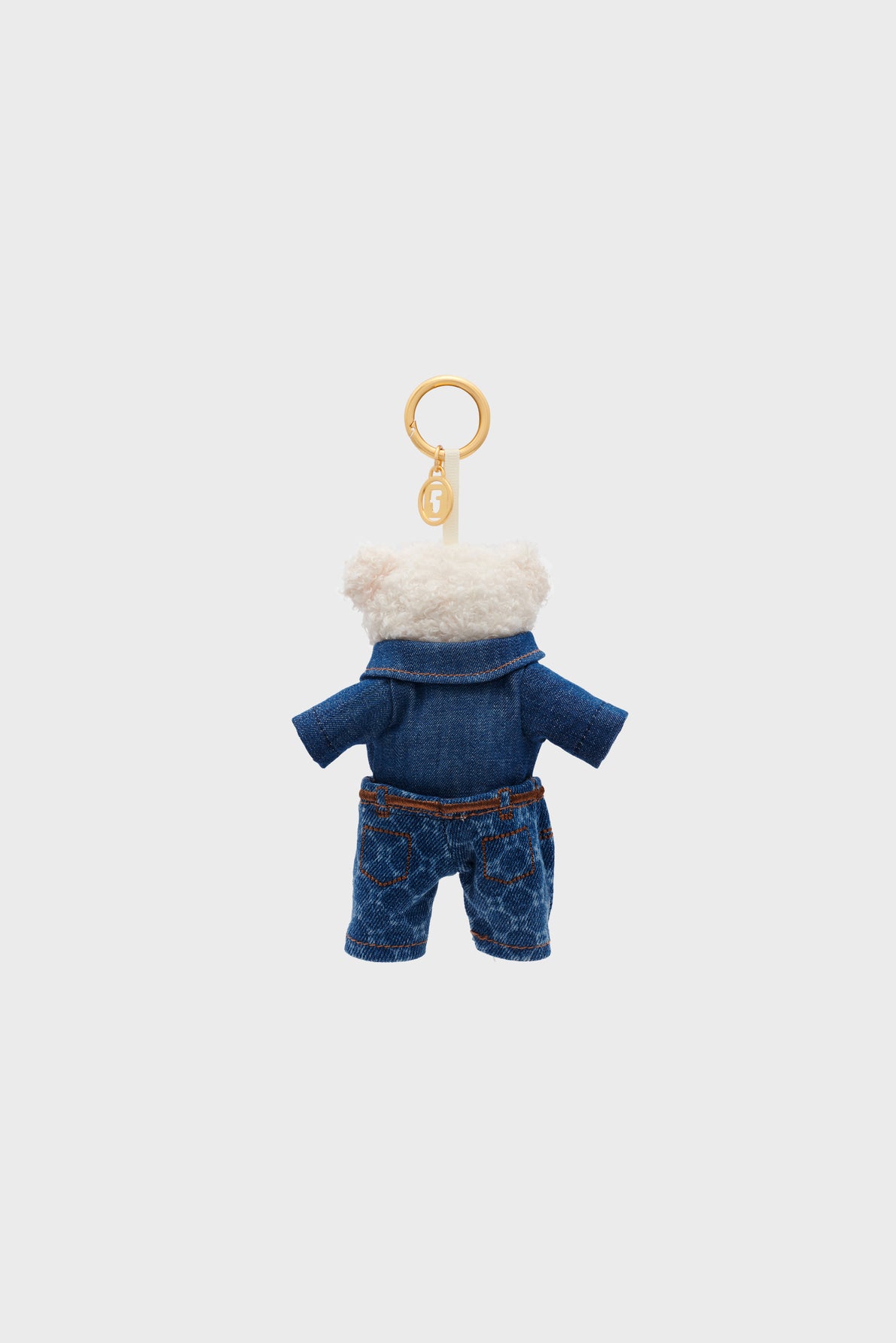 Plush teddy bear keychain, Darel charm peluche ourson, wearing a denim jacket and patterned blue jeans, hanging from a gold keyring—an irresistible accessoire mode shown against a plain white background.