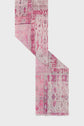 A pink and white patterned area rug, reminiscent of a foulard rose, is folded at a right angle on a plain light background, revealing various intricate designs and motifs in different shades of pink.