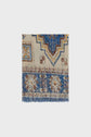 A square section of a woven rug with blue, beige, and brown geometric and floral patterns reminiscent of a motif ethnique, featuring fringed edges at the bottom—much like the intricate detailing found on an écharpe bohème or foulard Darina.