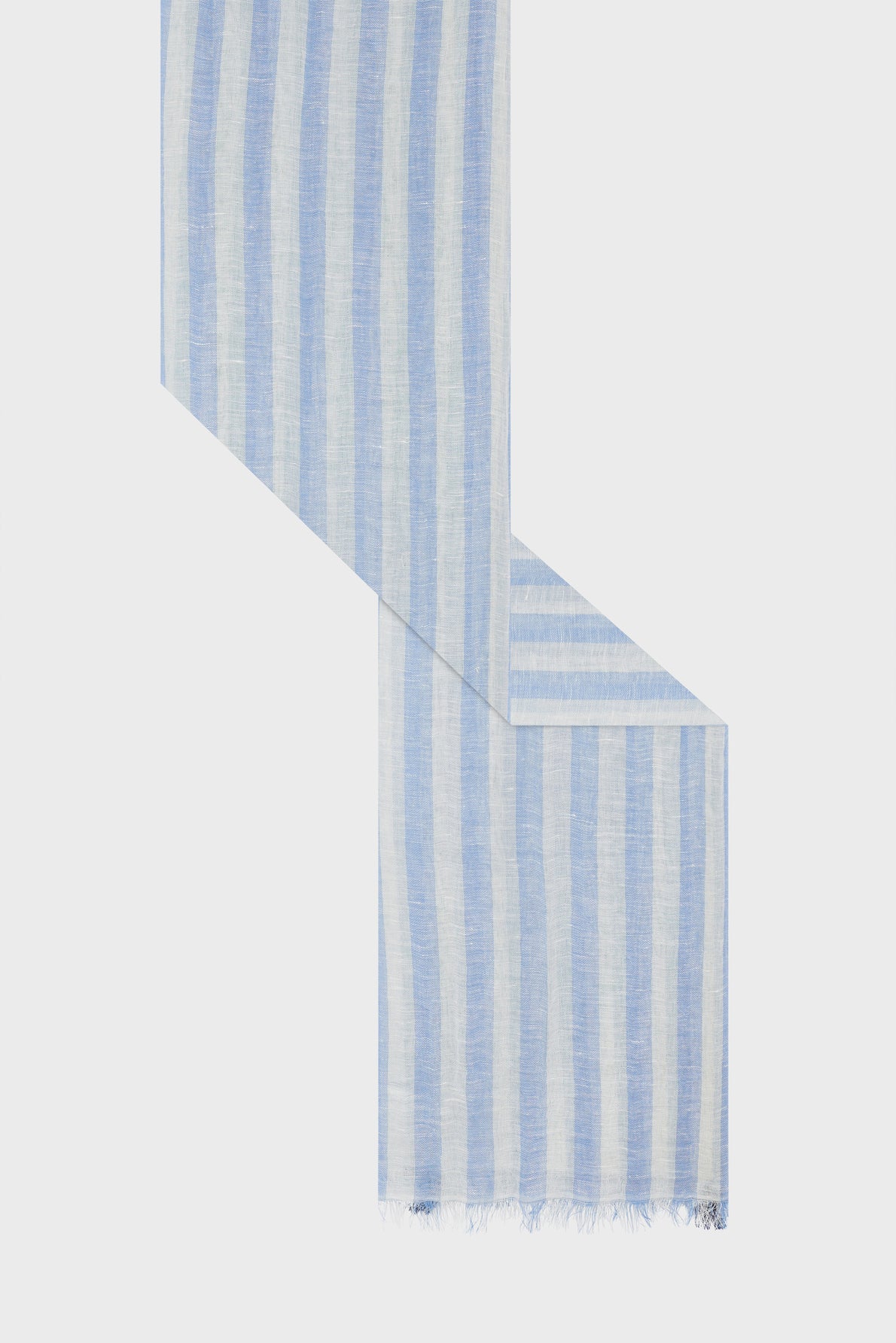 A long, lightweight étole rayée with vertical light blue and white stripes, arranged in a zigzag pattern. Crafted from a soft blend of coton et lin, the scarf features fringed edges on one end and is displayed on a plain white background.
