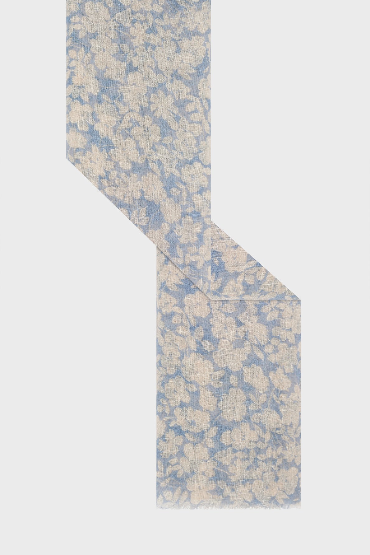 A light blue scarf with a beige floral pattern, or étole lin bleu ciel ornée d’un motif floral délicat, is displayed zigzagged on a plain white background.