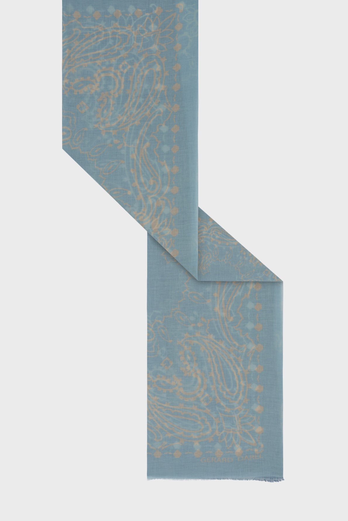 Light blue carré bandana scarf with a subtle beige paisley pattern, shown folded at an angle against a plain white background. The lightweight coton fabric features slightly frayed edges at the bottom, enhancing its effortless charm.
