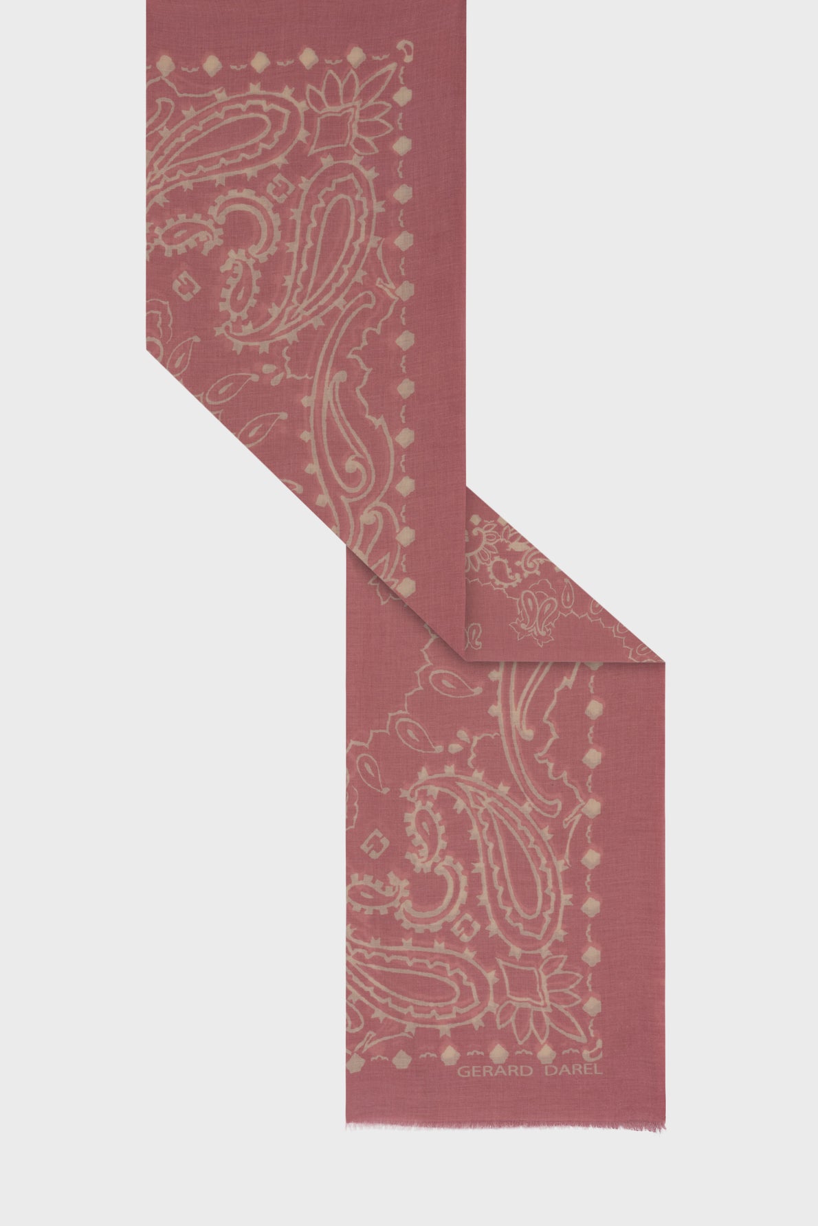 Dusty rose pink carré bandana-style scarf in soft coton with a cream paisley motif géométrique and frayed edges, partially folded on a light background. The words Gerard Darel are printed in the corner.