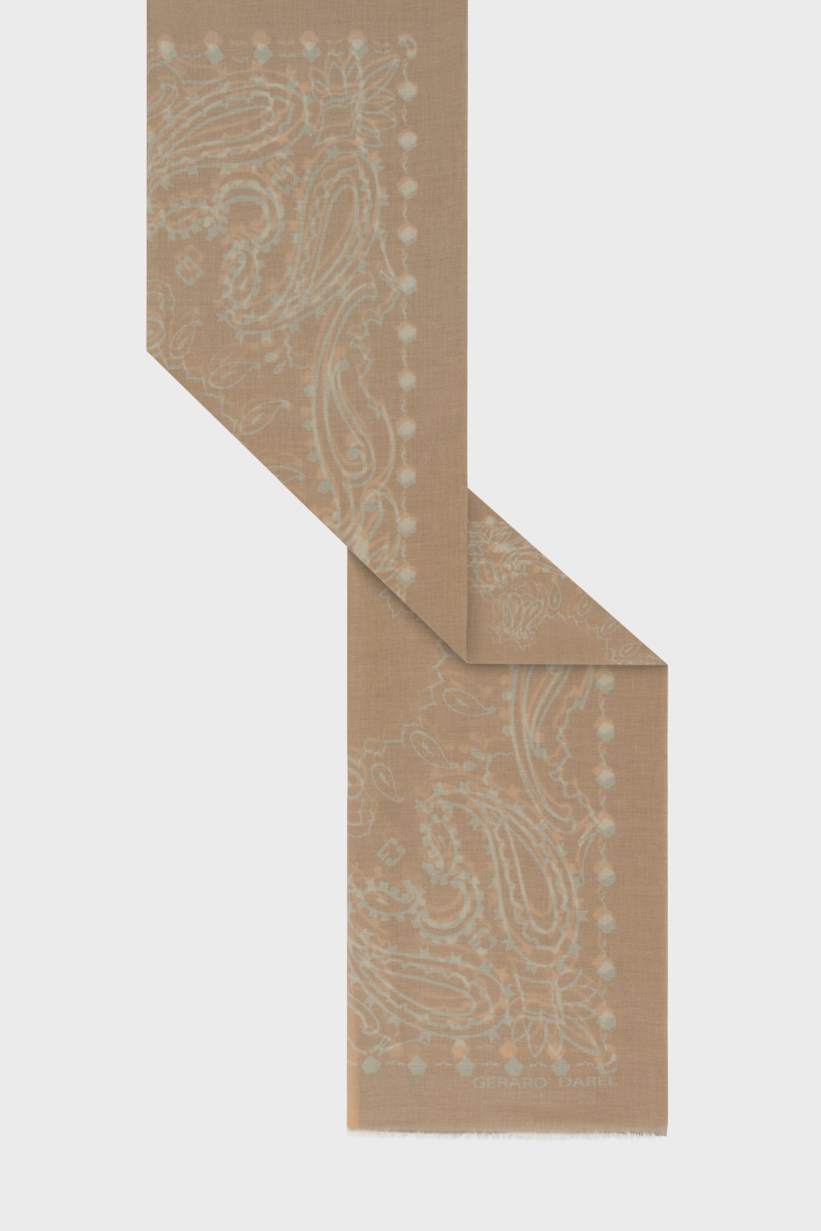 Light brown scarf with a light blue paisley pattern and subtle dotted border, folded at an angle in the style of a carré coton. The fabric appears soft and lightweight, complemented by a touch of motif géométrique for added visual interest. The brand name Gerard Darel is printed at the bottom edge.