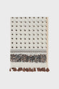 A cream-colored étole Daphné with a small brown floral pattern, a decorative border featuring intricate brown and black designs, and brown tassels along the edge. Crafted in a luxurious blend of coton et soie, this élégante étole florale adds effortless sophistication to any ensemble.