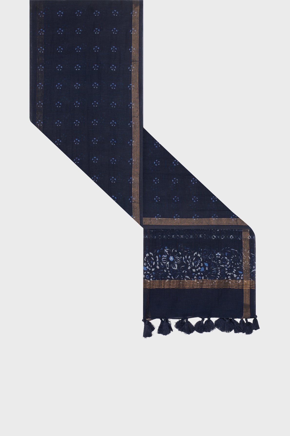 A navy blue scarf with small light blue floral patterns—a subtle imprimé floral—features gold-bordered edges, a broader pattern near one end, and dark blue tassels hanging from the end. Crafted in a luxurious blend of coton et soie, this étole Daphné brings elegance to any ensemble.