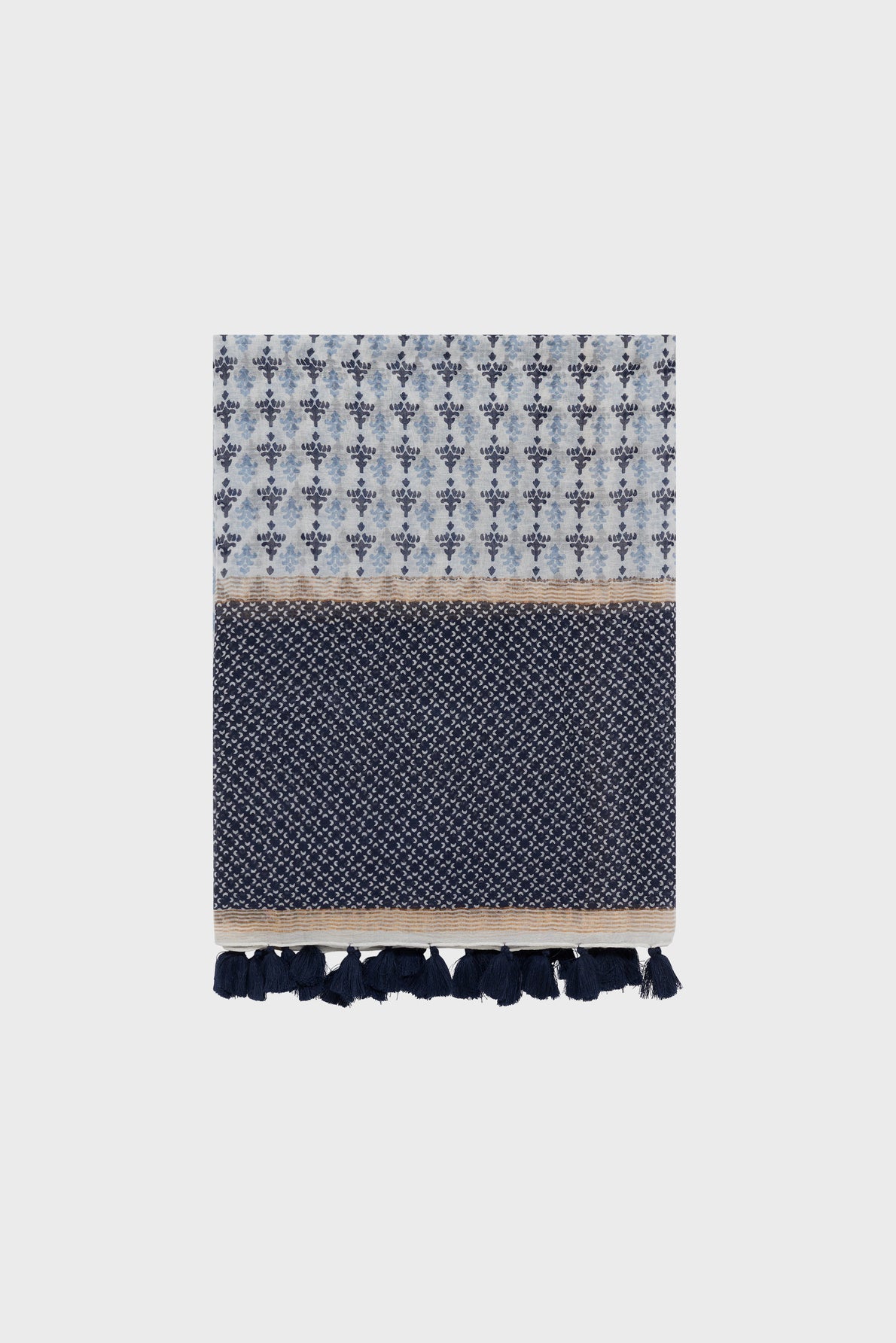 A folded blue and white patterned towel with motifs géométriques, a beige accent stripe, and navy blue tassels along the bottom edge, crafted from a luxurious blend of coton et soie and displayed on a plain light background.