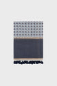 A folded blue and white patterned towel with motifs géométriques, a beige accent stripe, and navy blue tassels along the bottom edge, crafted from a luxurious blend of coton et soie and displayed on a plain light background.