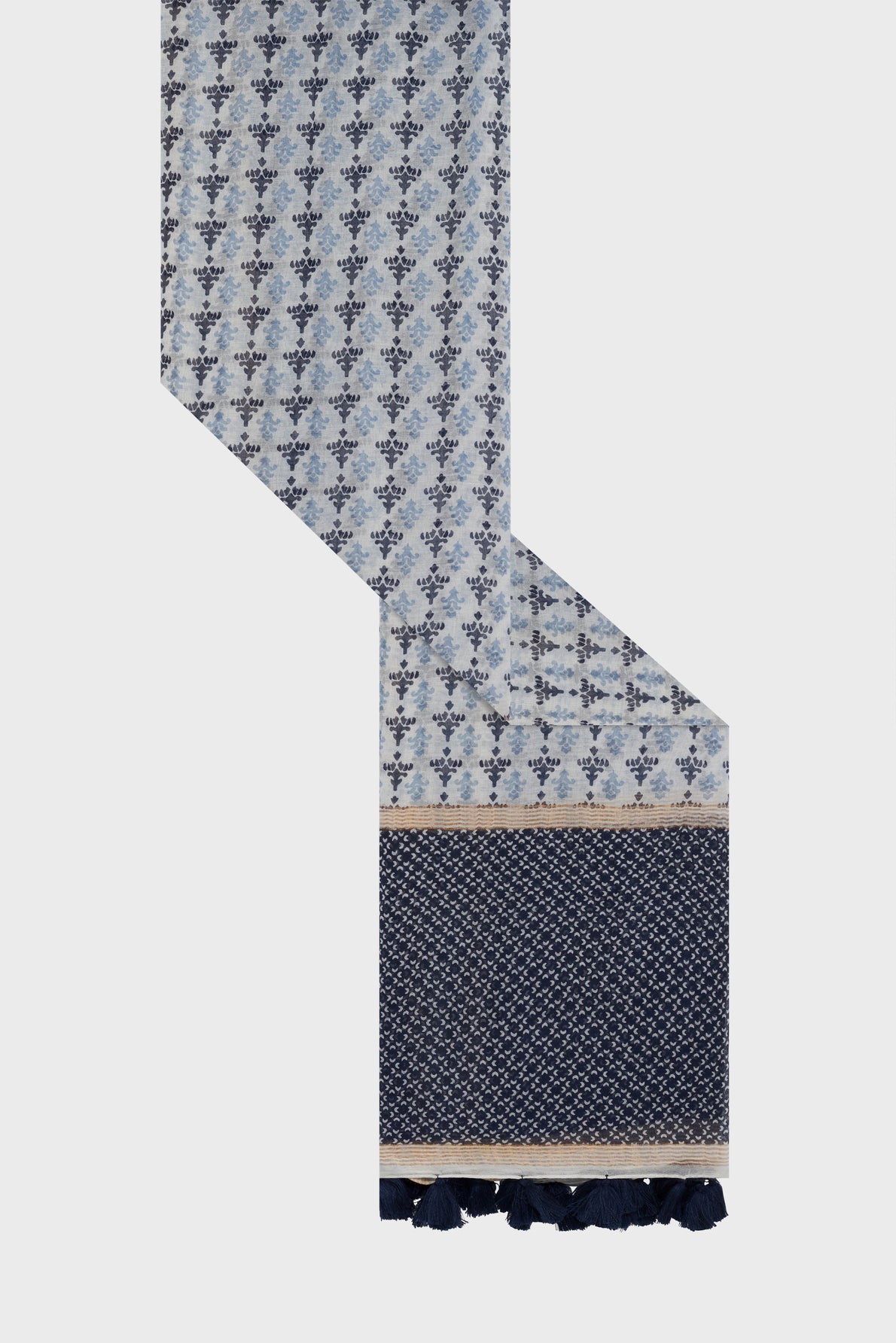 A long blue patterned foulard Dalma with small floral motifs and motifs géométriques, featuring a solid dark blue section with white dots, elegant beige borders, and dark blue tassels at the end. Crafted from a luxurious blend of coton et soie, this scarf is displayed against a plain background.